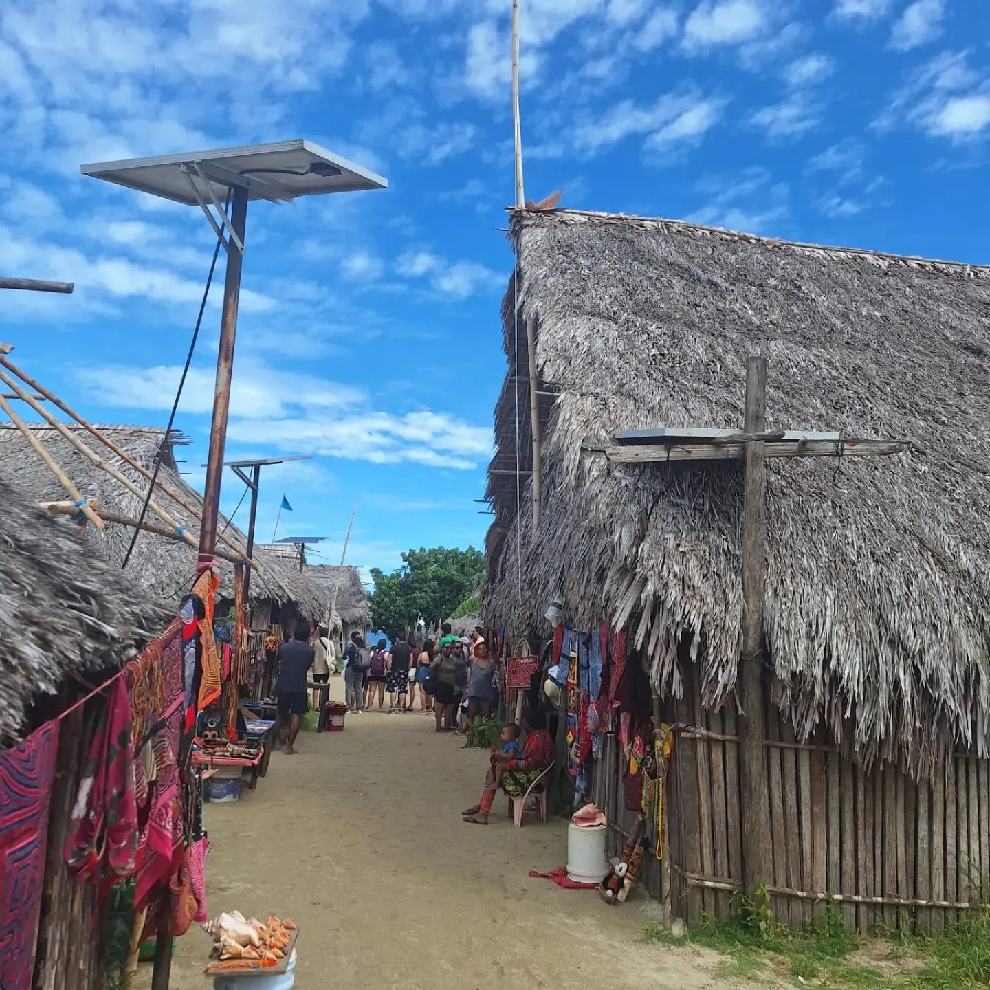 A sandy lane between thatched Guna houses with colorful molas on display