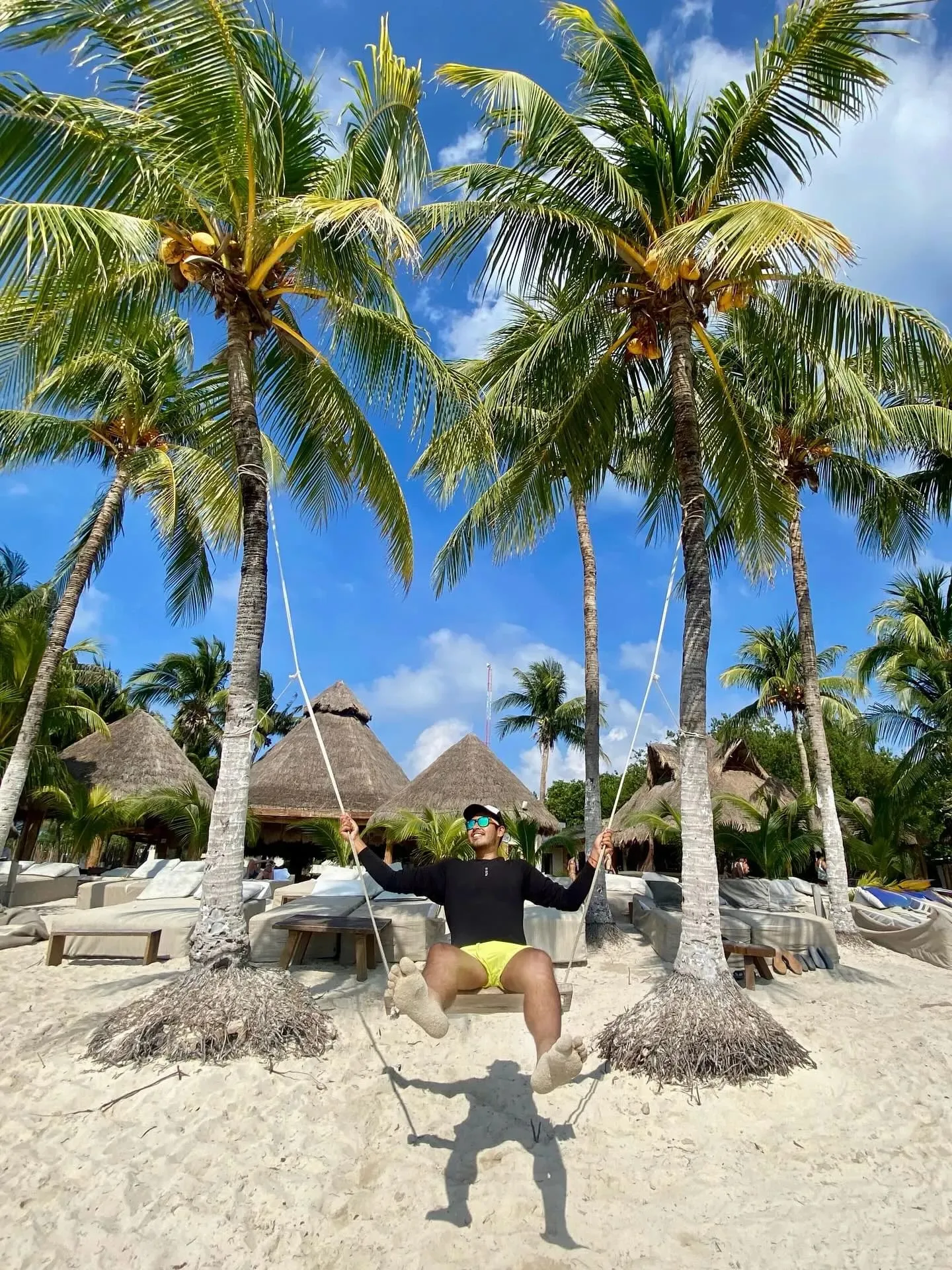 A traveler on a rope swing under the palms next to thatched huts on a San Blas island