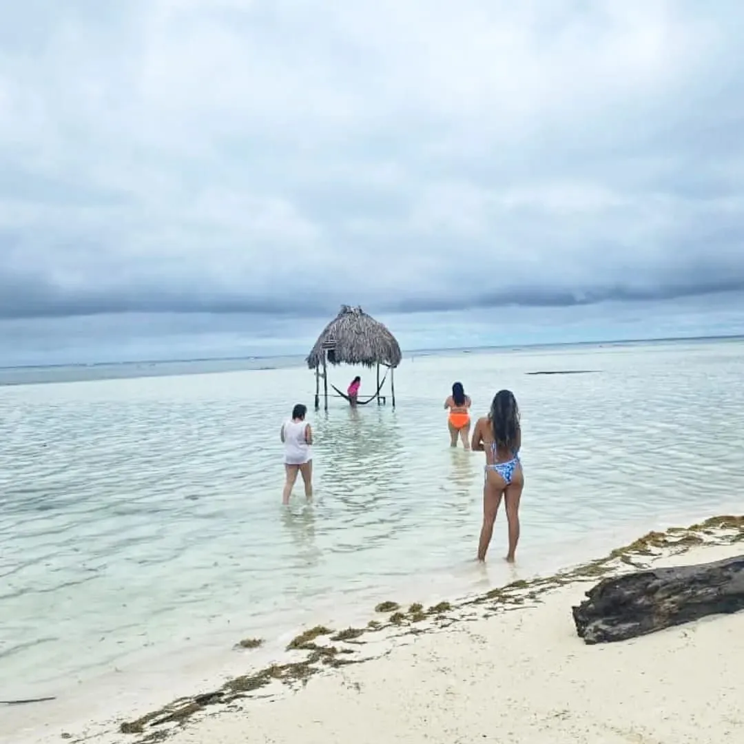 Viajeros caminando por agua mansa y poco profunda hacia un pequeño refugio de paja en Guna Yala