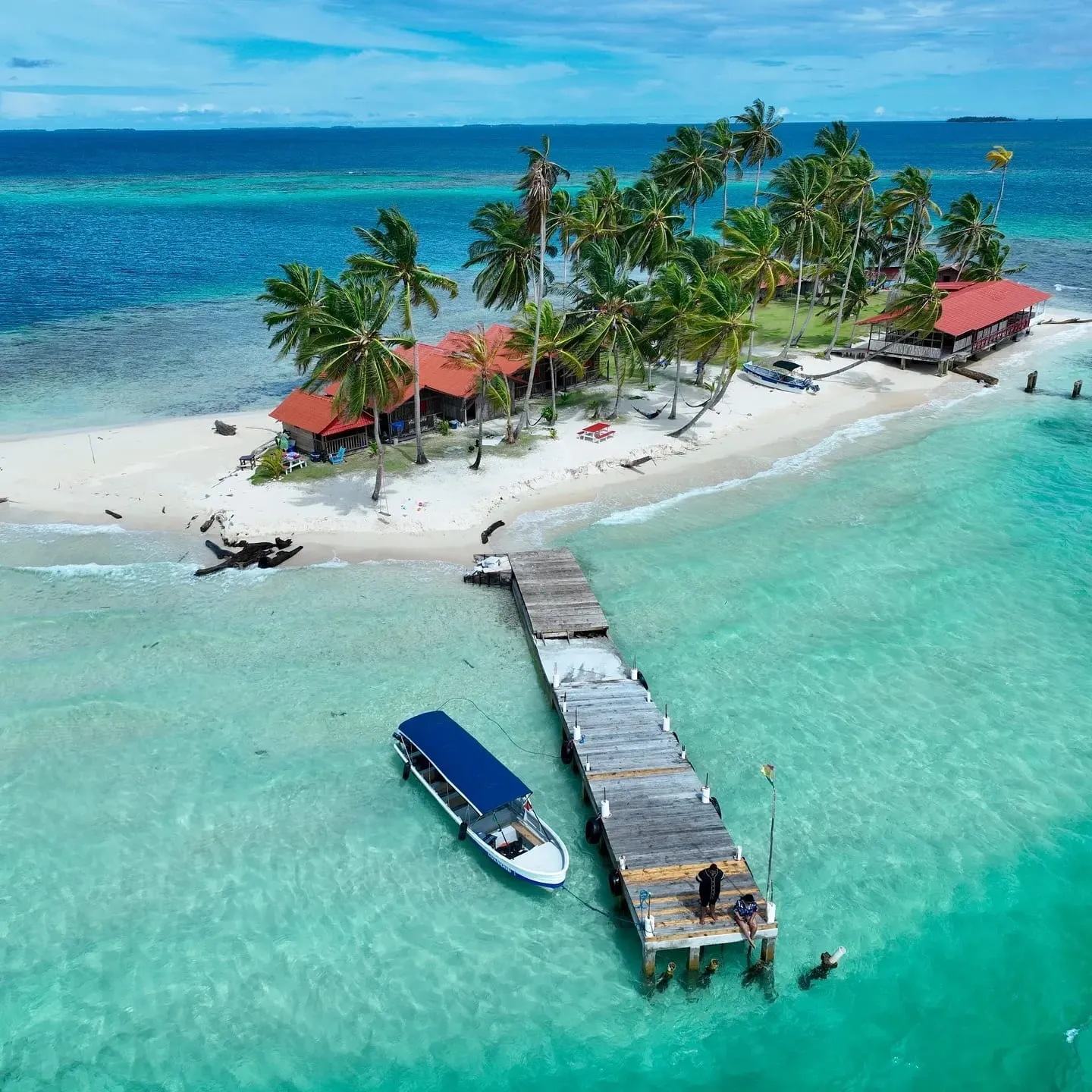 Vista aérea de una pequeña isla de Guna Yala con muelle de madera y un bote amarrado en agua turquesa
