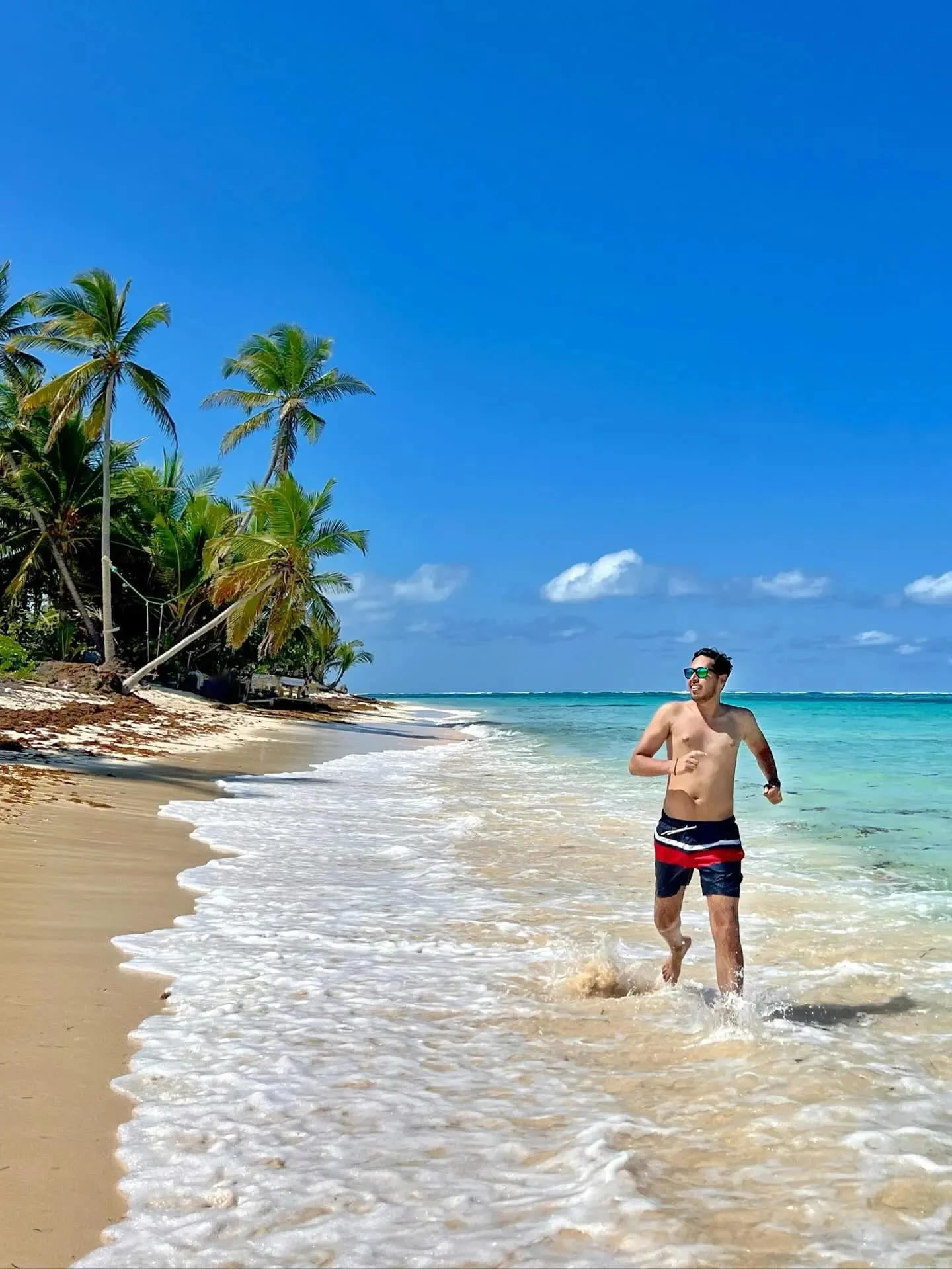 A traveler walking along the water's edge on a palm-lined beach in Guna Yala