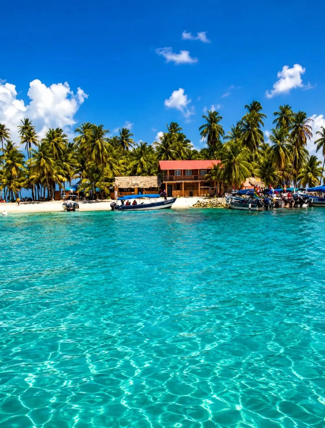 Cabañas sencillas y pequeñas lanchas en una isla rodeada de agua turquesa en Guna Yala
