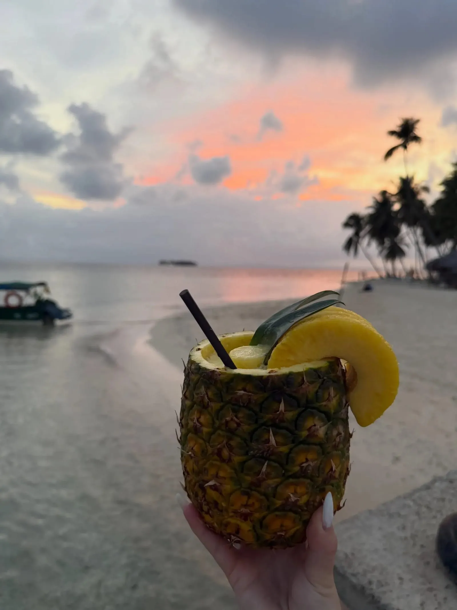 Una piña colada servida en una piña vaciada, sostenida frente al mar y las palmeras