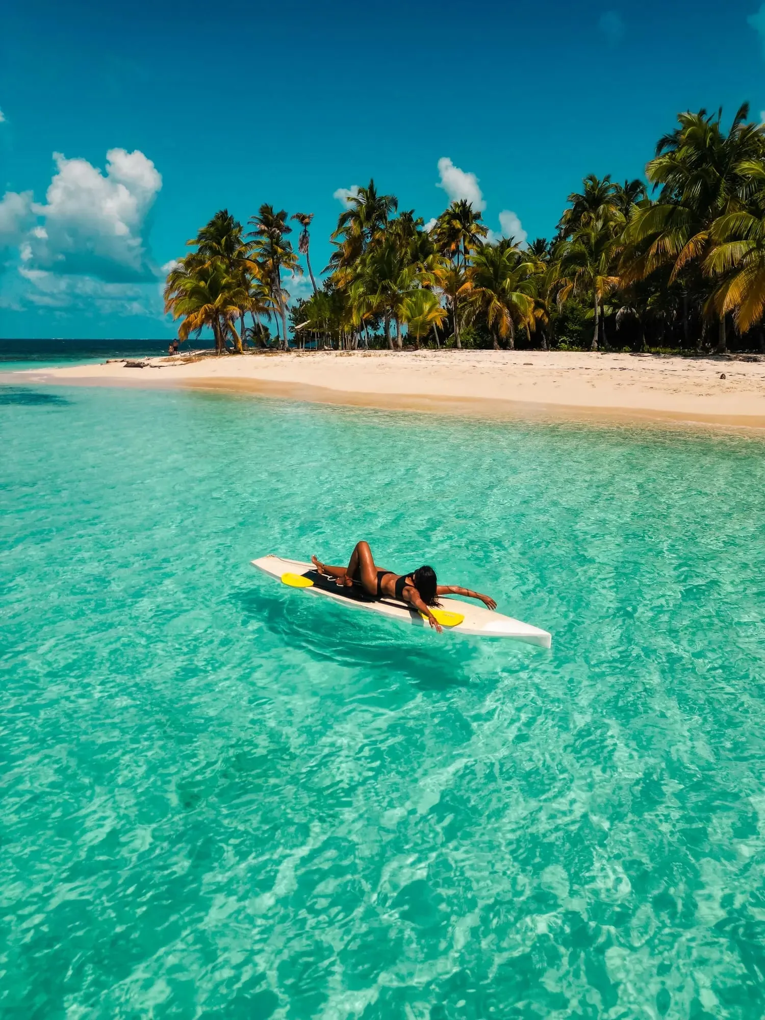 Viajera sobre una tabla de paddle en agua turquesa cristalina frente a una isla con palmeras en Guna Yala